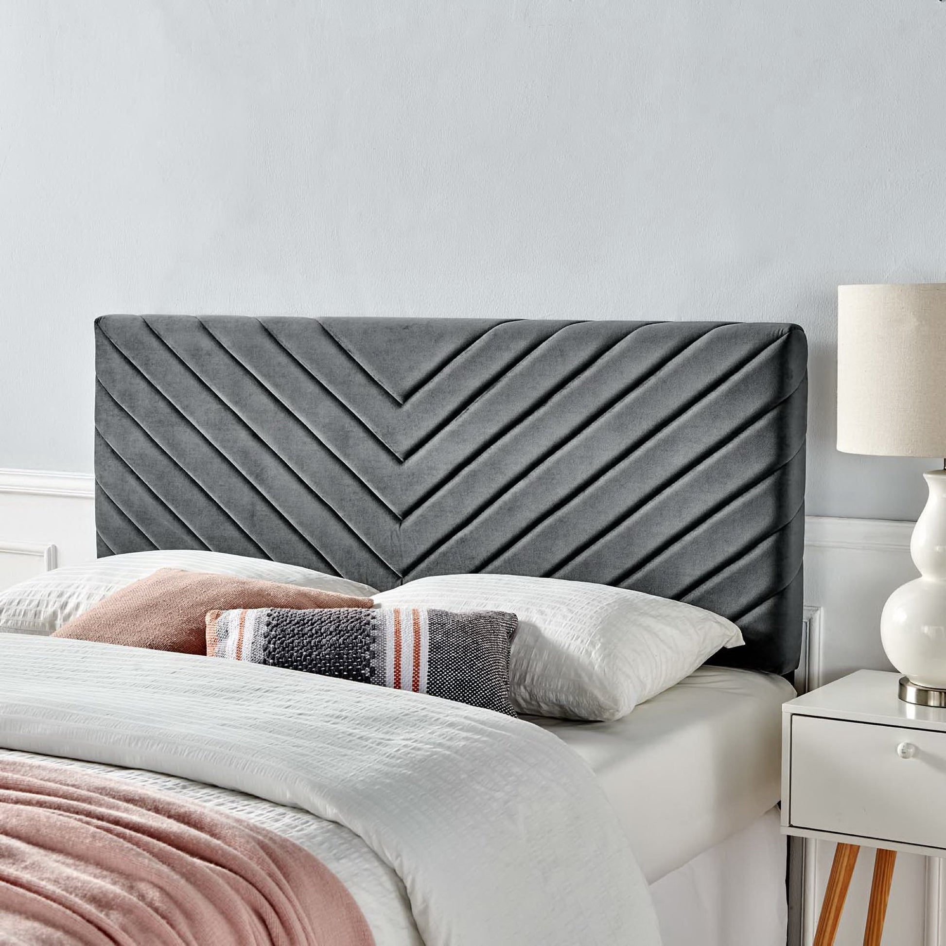 Dark gray angular channel-tufted headboard with white bedding and pink throw, modern bedroom setup with nightstand lamp