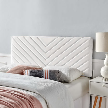 White upholstered headboard with angular channel tufting, shown with bed linens, pink throw, striped pillow, & white nightstand with a beige lamp.