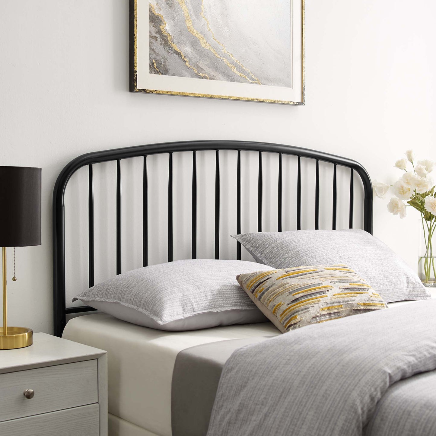 Black metal arched headboard with vertical slats on a gray bed; yellow-gray striped accent pillow, bedside lamp.