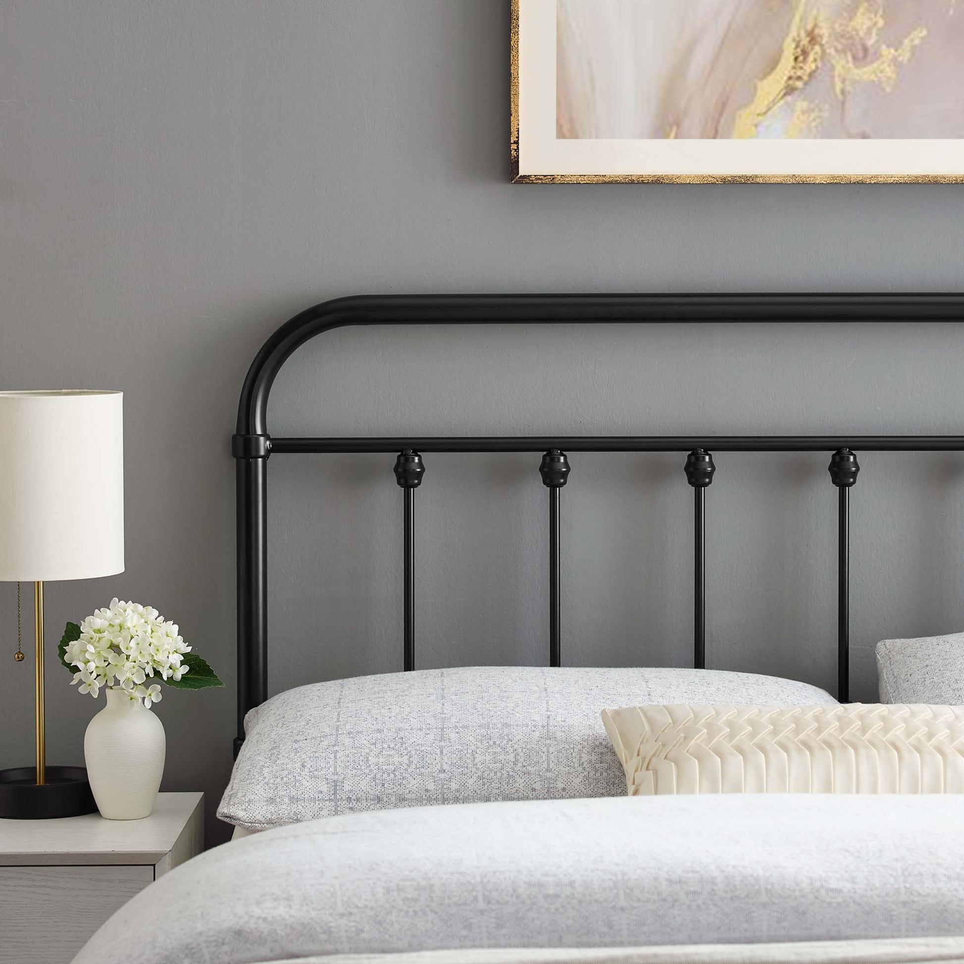 Black metal headboard with a curved top and slim vertical bars, gray bedding and a cream decorative pillow