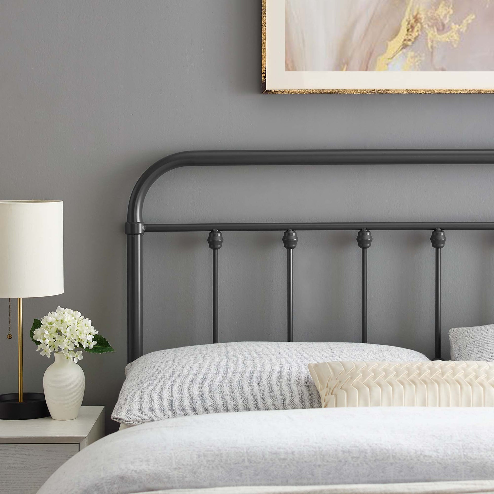 Dark metal king headboard with curved top and vertical spindles, grey bedding, white nightstand, lamp, and vase.