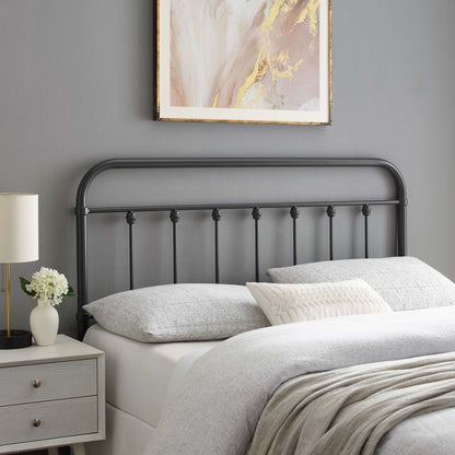 Gray metal king headboard with a curved top and vertical spindles, gray bedding, throw blanket, white pillows, with a nightstand and lamp.