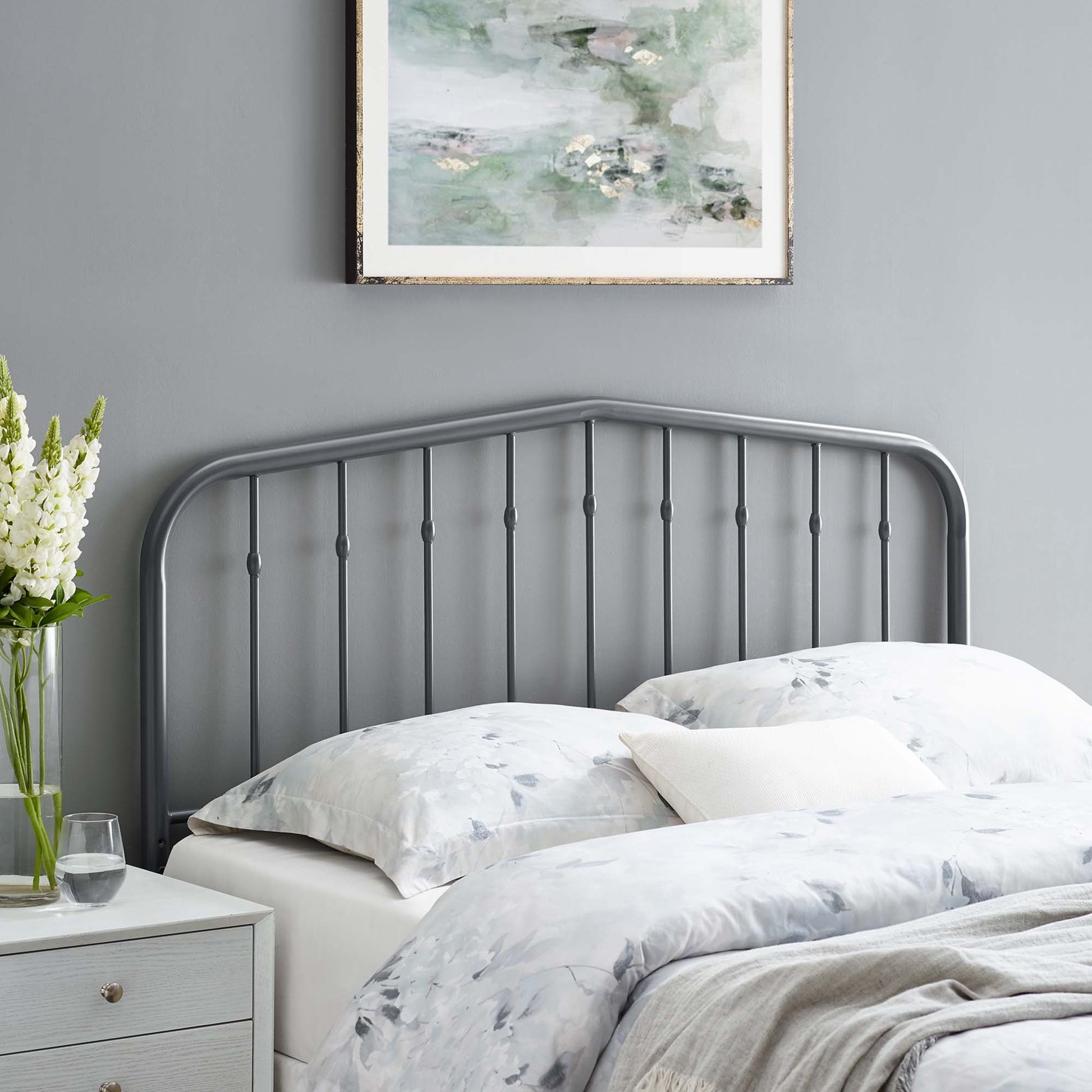 Gray metal headboard with curved top and vertical spindles, light floral bedding, white nightstand and vase of flowers.