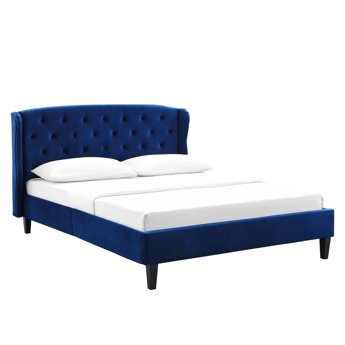 Navy blue velvet platform bed with tufted wingback headboard and dark tapered legs, dressed in white bedding.