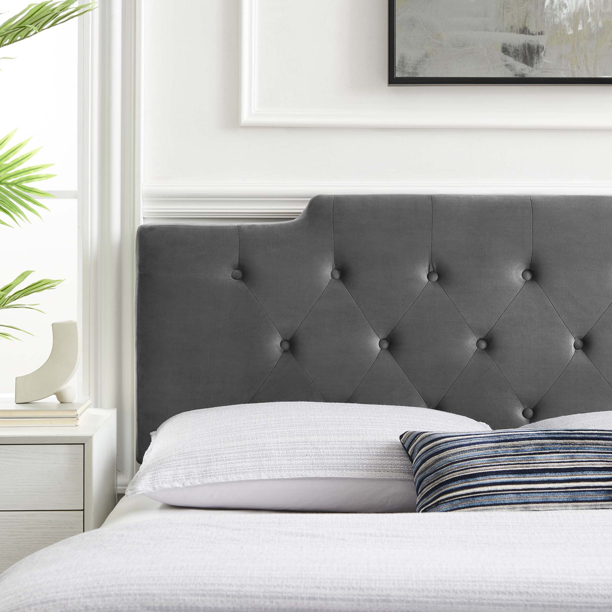 Gray tufted headboard with button tufting in a white-walled bedroom; white bedding & a striped pillow.