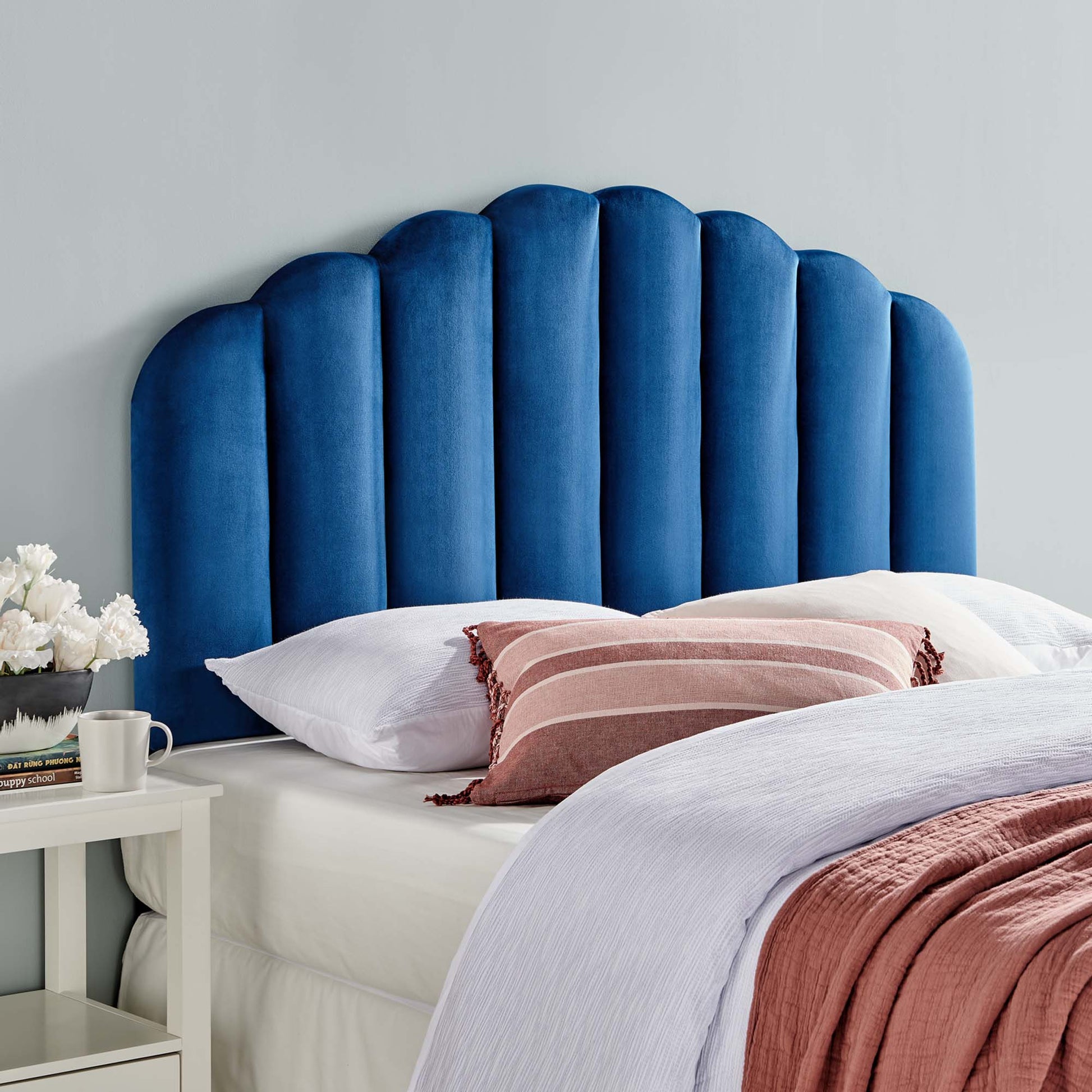 Blue velvet scalloped headboard with white bedding and dusty pink throw pillows in a cozy modern bedroom.
