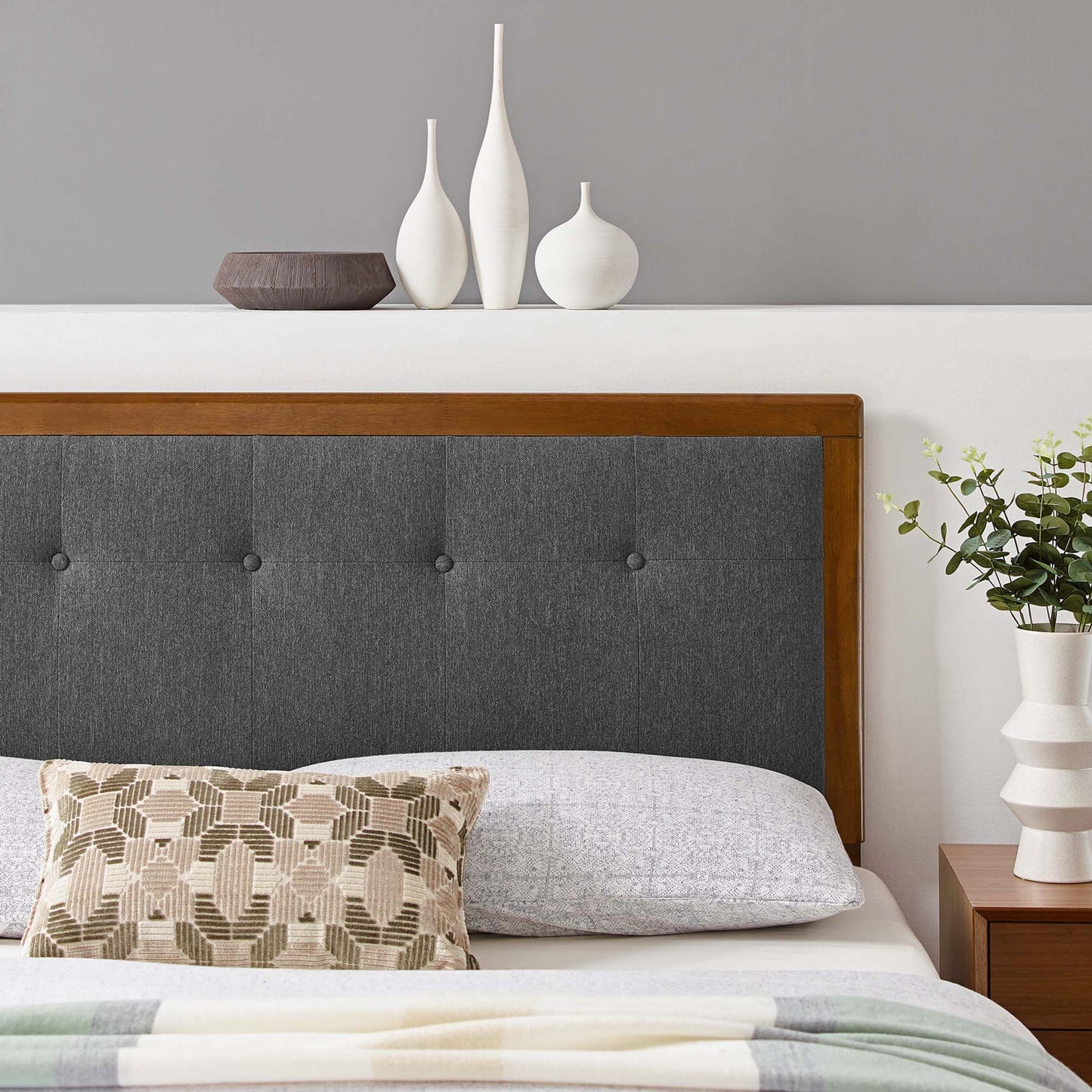 Walnut-framed charcoal gray tufted king headboard with geometric beige pillow and light bedding.