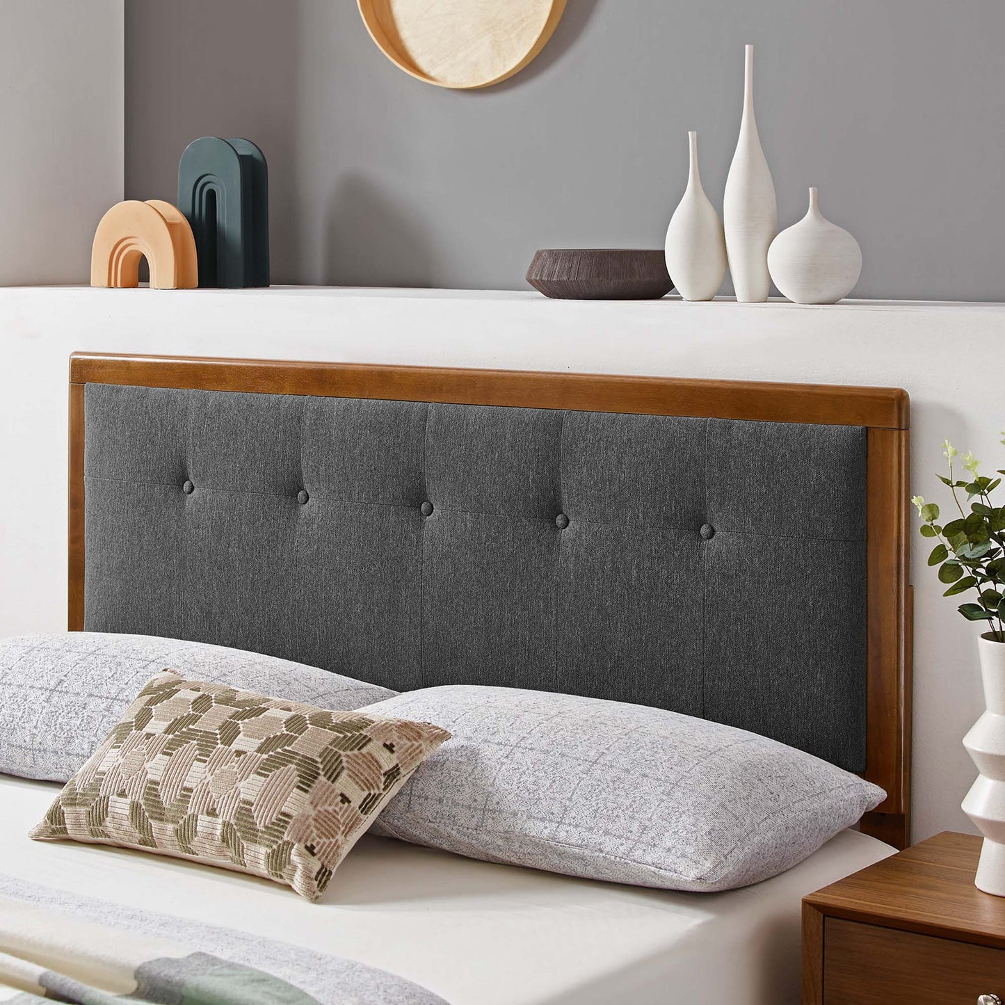 Black tufted fabric headboard with wood frame, gray bedding, and a beige-green geometric throw pillow.