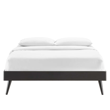 Black modern platform bed with a low rectangular frame and angled tapered legs, dressed in white sheets and pillows.