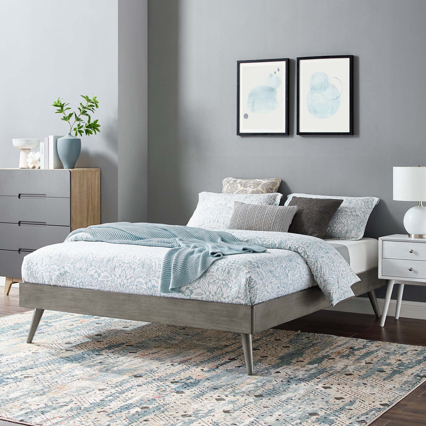 Gray platform bed with blue patterned bedding and cozy throw in a modern gray bedroom with abstract art.