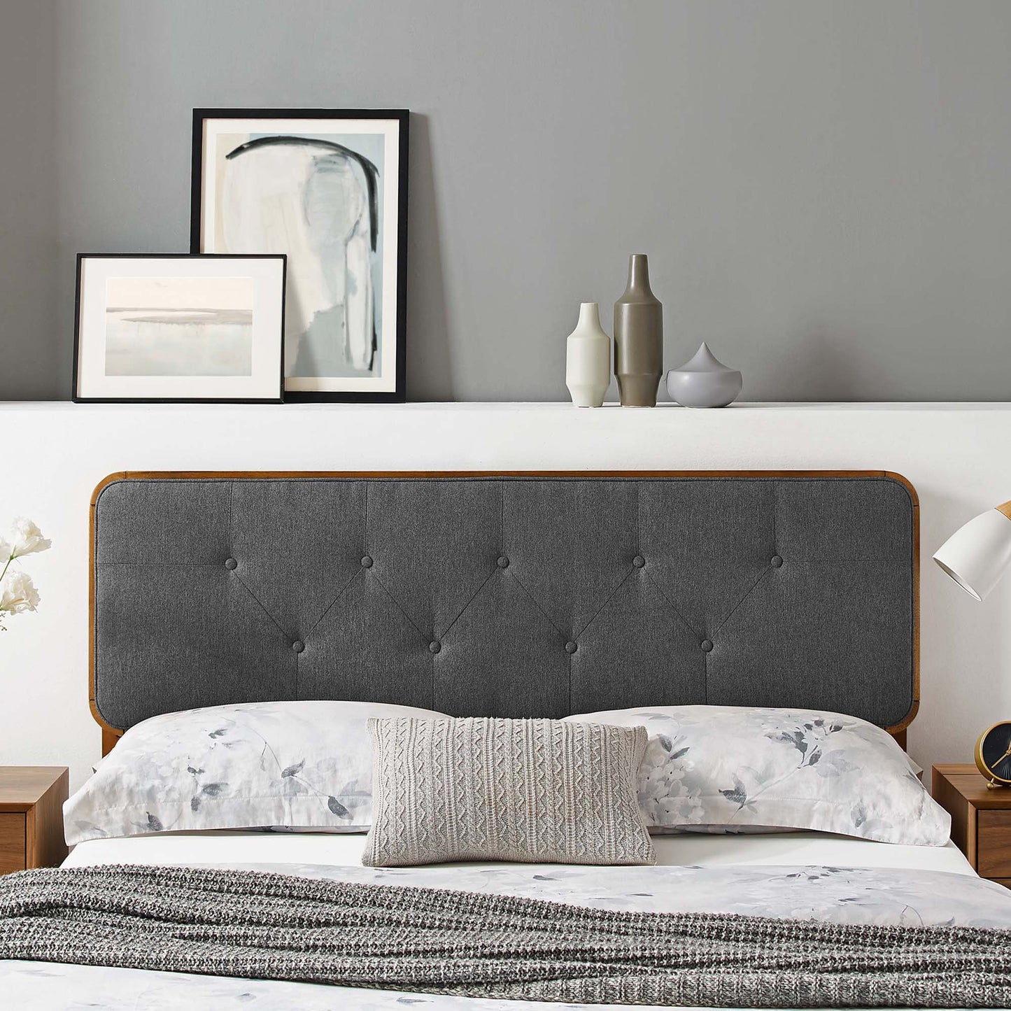 Black tufted fabric-and-wood headboard on a bed; floral sheets, knitted pillow, and knitted throw; modern bedroom scene with wall art.