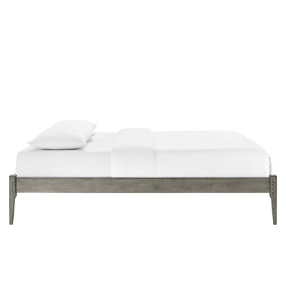 Low-profile platform bed with weathered gray wood frame and white sheets and pillows, industrial minimalist style.