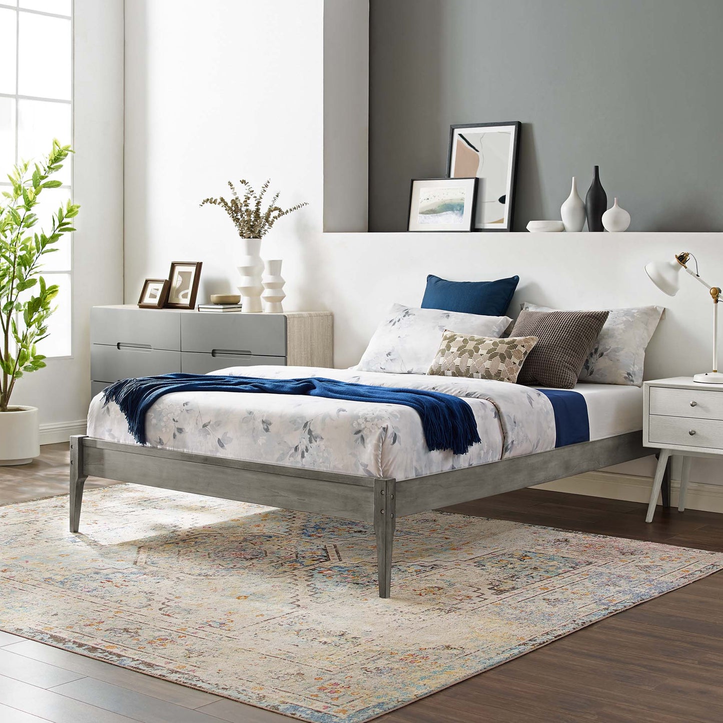 Gray wood queen platform bed frame with floral bedding and blue accents; contemporary bedroom with dresser, rug, and plant.