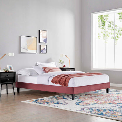 Burgundy upholstered platform bed with white linens, rust throw, black nightstands, abstract art, and a colorful rug.