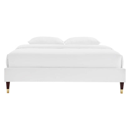 White velvet-upholstered platform bed with four tapered legs ending in brass caps; modern minimalist bedroom staple.