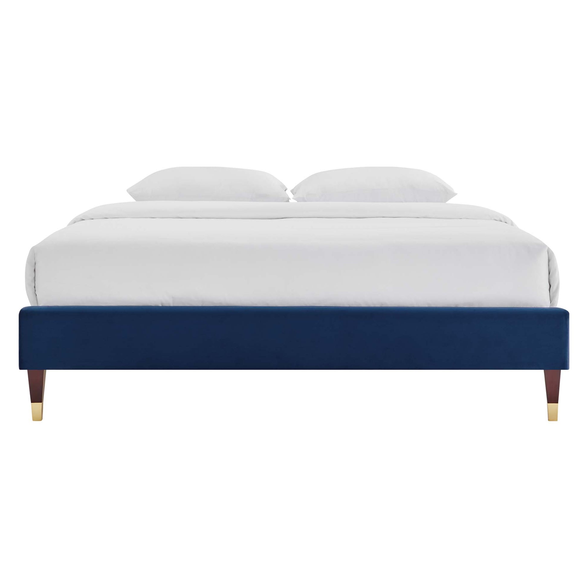 Navy blue velvet platform bed with tapered wooden legs and gold caps, dressed in white bedding.