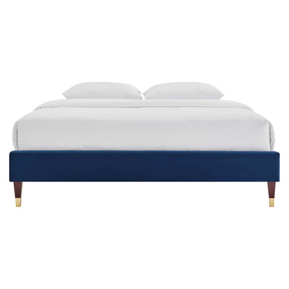 Navy blue velvet platform bed with tapered wooden legs and gold caps, dressed in white bedding.