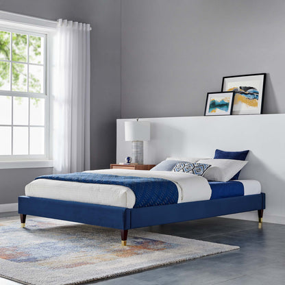 Navy blue upholstered platform bed with white headboard, gold-tipped legs and blue-and-white bedding in a modern gray bedroom.