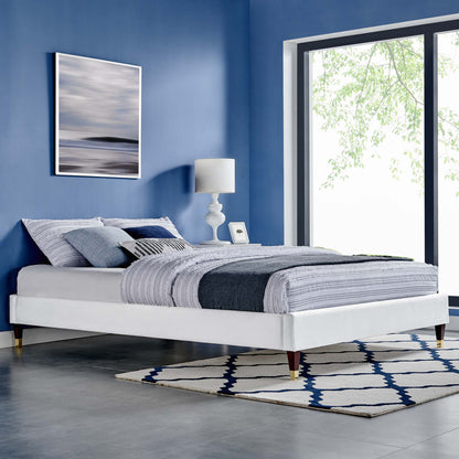 White platform bed with blue-gray quilt, wooden tapered legs, blue walls, large window, and navy geometric rug.
