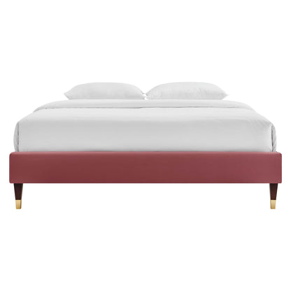 Maroon upholstered platform bed with gold-tipped wooden legs, white bedding and two pillows.