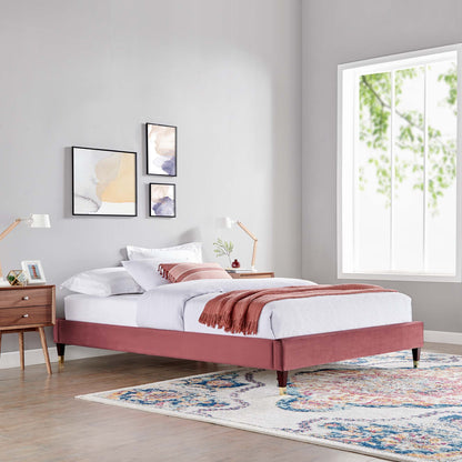 Dusty-rose upholstered platform bed with tapered legs, white linens, pink throw, in a gray modern bedroom with a colorful rug.
