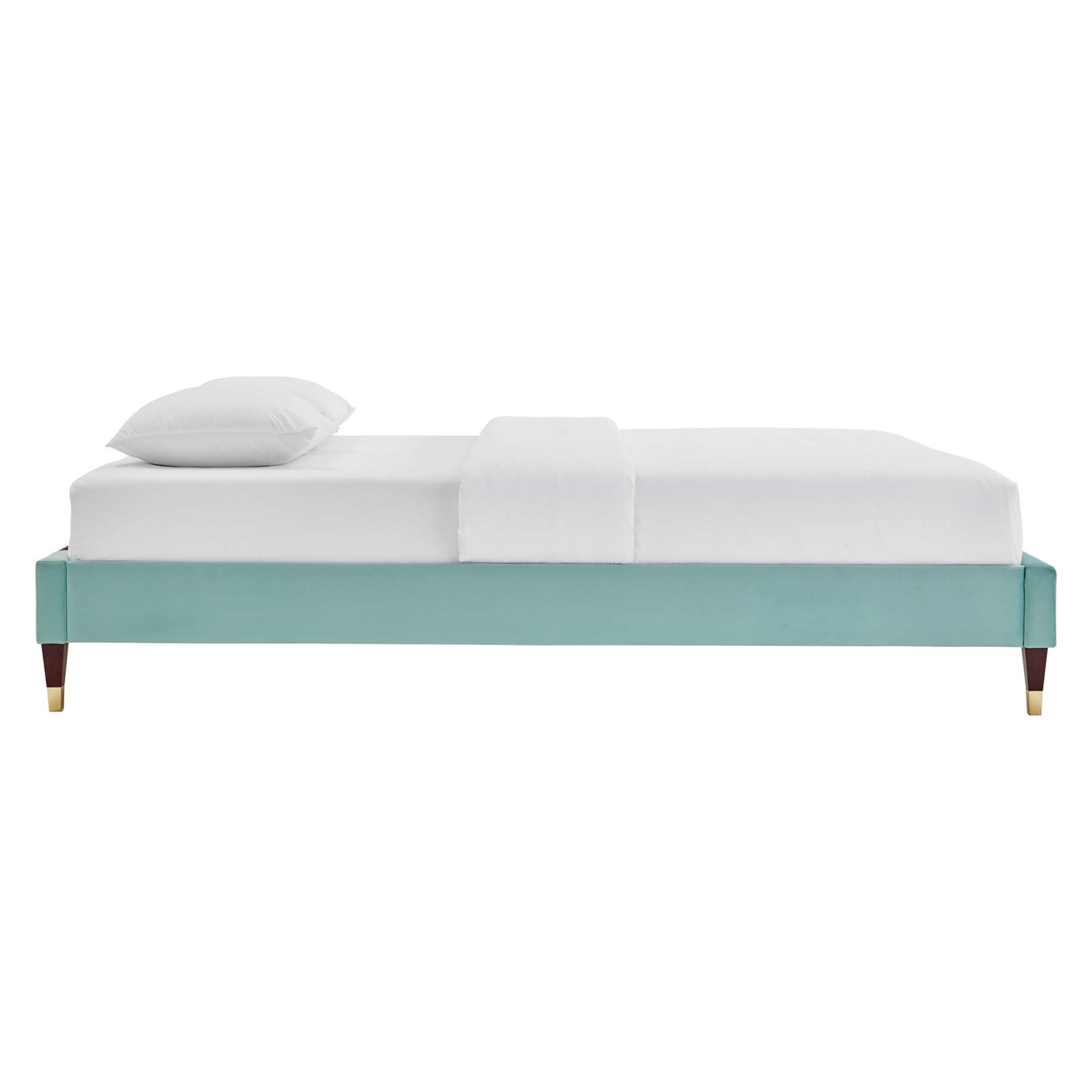 Mint green upholstered platform bed frame with tapered wooden legs and brass caps, white bedding.