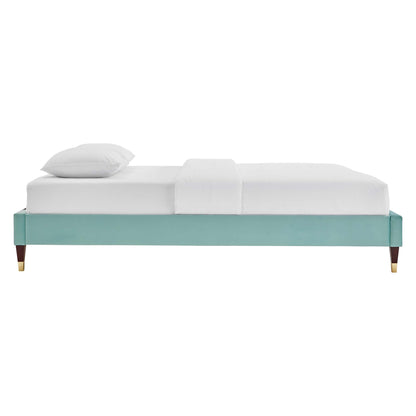 Mint green upholstered platform bed frame with tapered wooden legs and brass caps, white bedding.