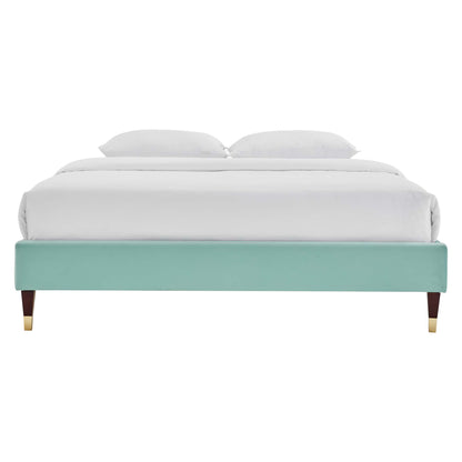 Mint teal upholstered platform bed with tapered wooden legs & gold caps, white bedding.