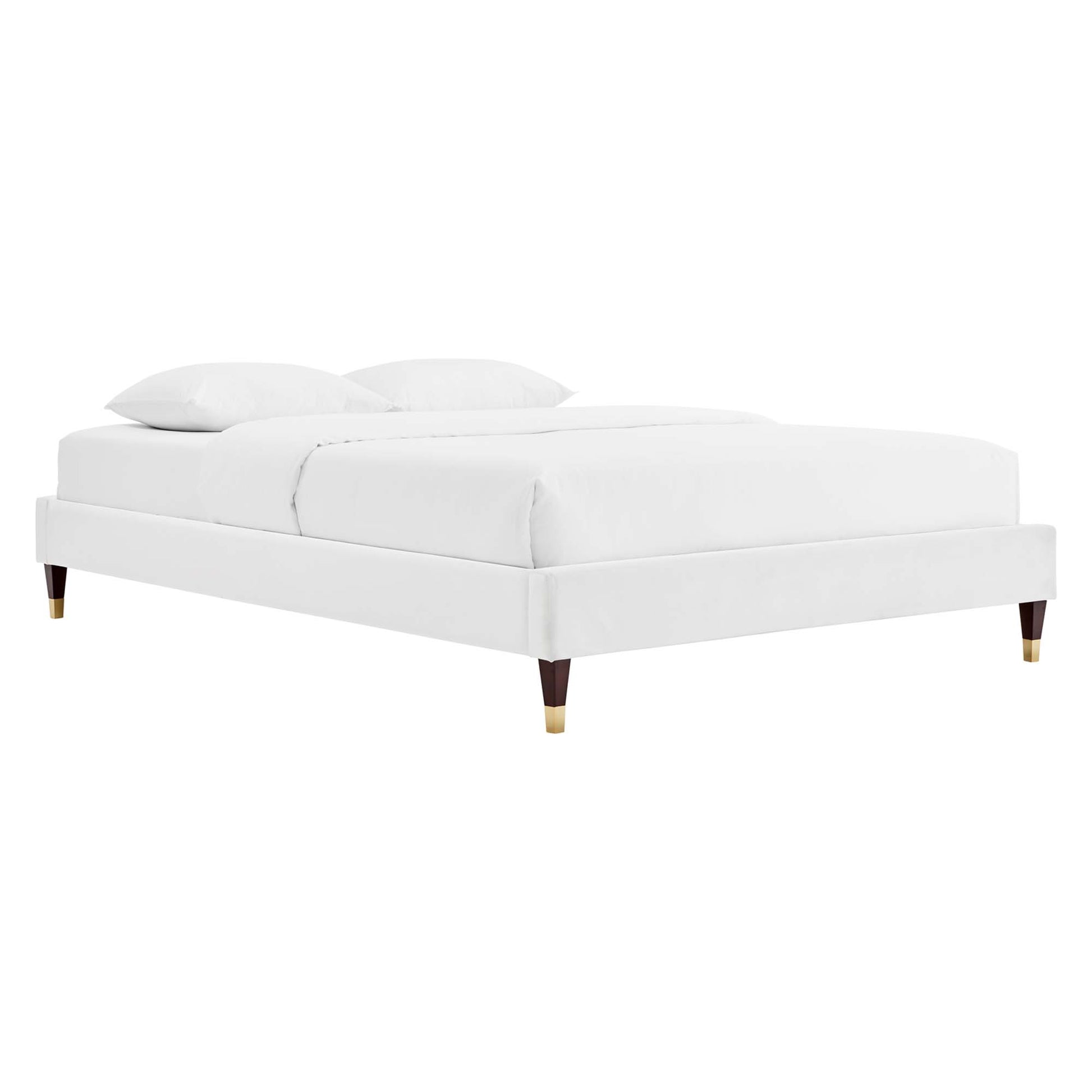 White upholstered platform bed with a low-profile frame, tapered wooden legs with brass caps, and white bedding with two pillows.