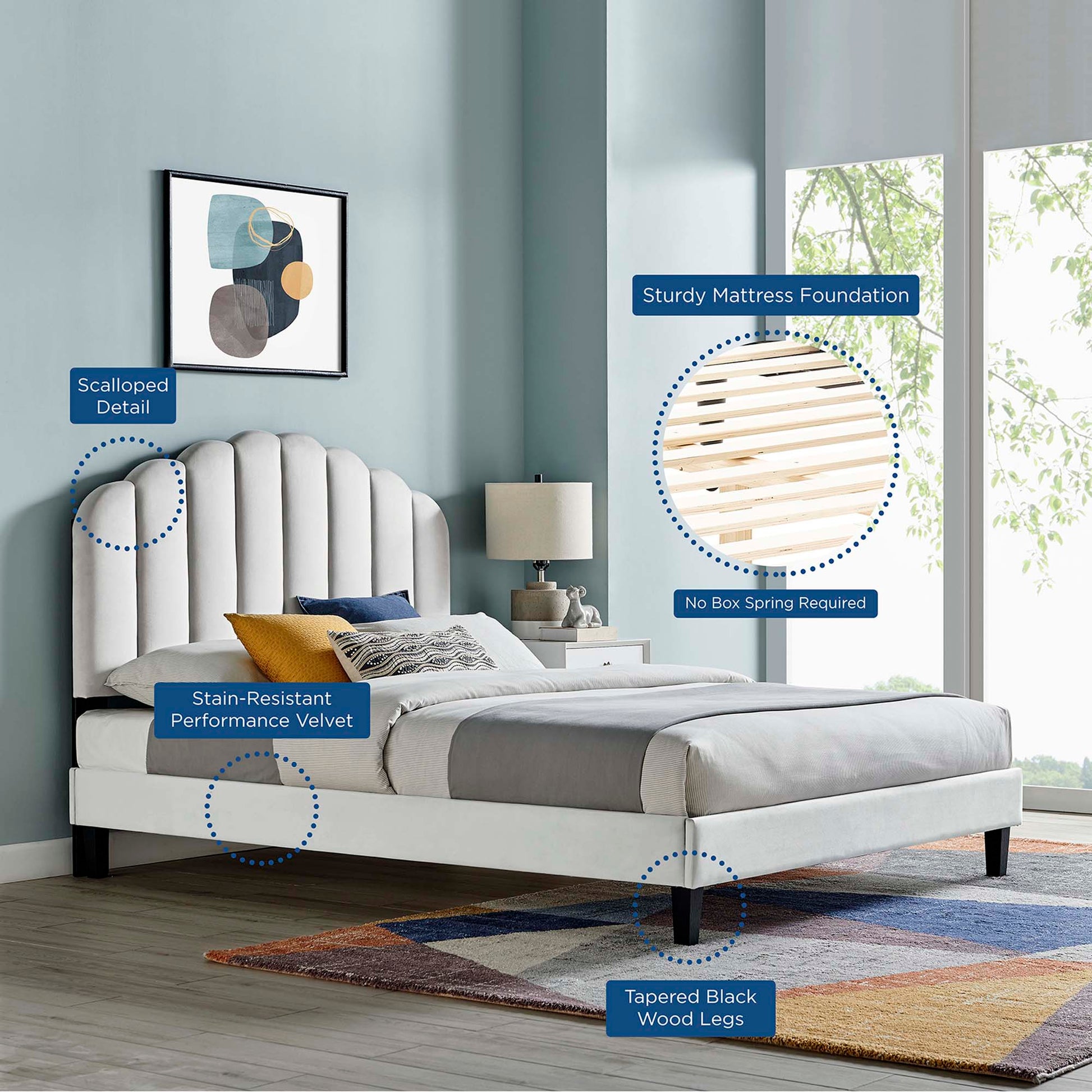 Light gray velvet upholstered platform bed with scalloped headboard and tapered black wood legs in a blue-toned bedroom.
