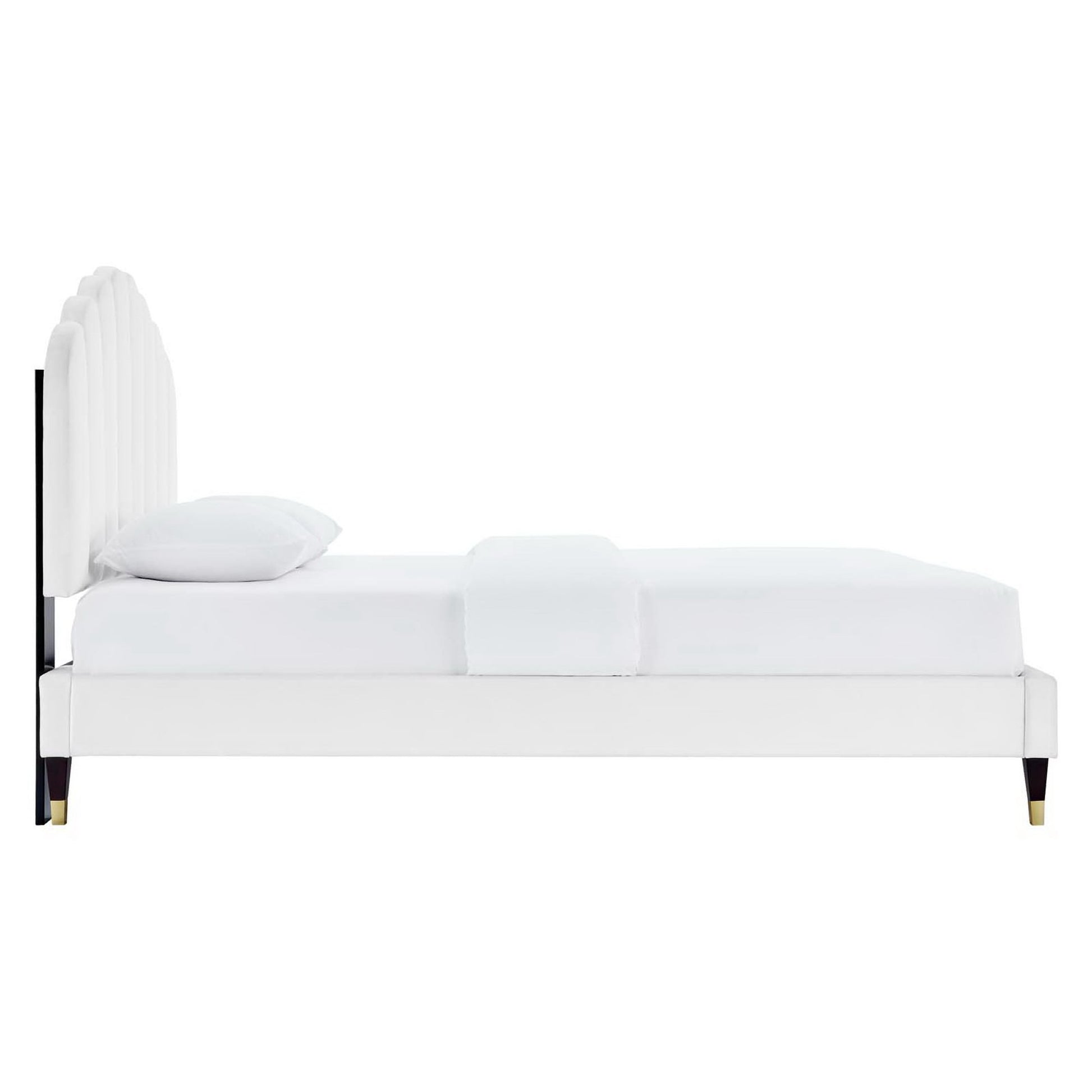 White upholstered platform bed with tall curved headboard, white bedding, and dark tapered legs with brass caps.