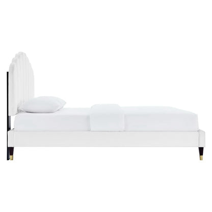 White upholstered platform bed with tall curved headboard, white bedding, and dark tapered legs with brass caps.