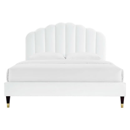 White upholstered platform bed with a tall scalloped shell headboard and gold-tipped legs.