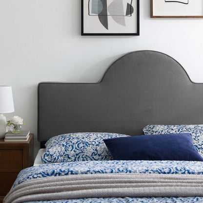 Grey curved upholstered twin headboard with blue paisley bedding, navy throw pillow, wooden nightstand, lamp and framed art.