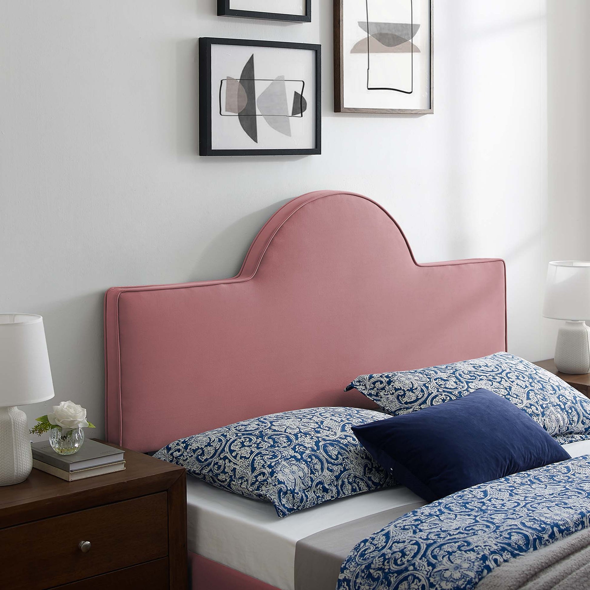 Dusty rose velvet twin headboard with curved crown; blue paisley bedding & navy pillows, dark wood nightstand, abstract wall art.