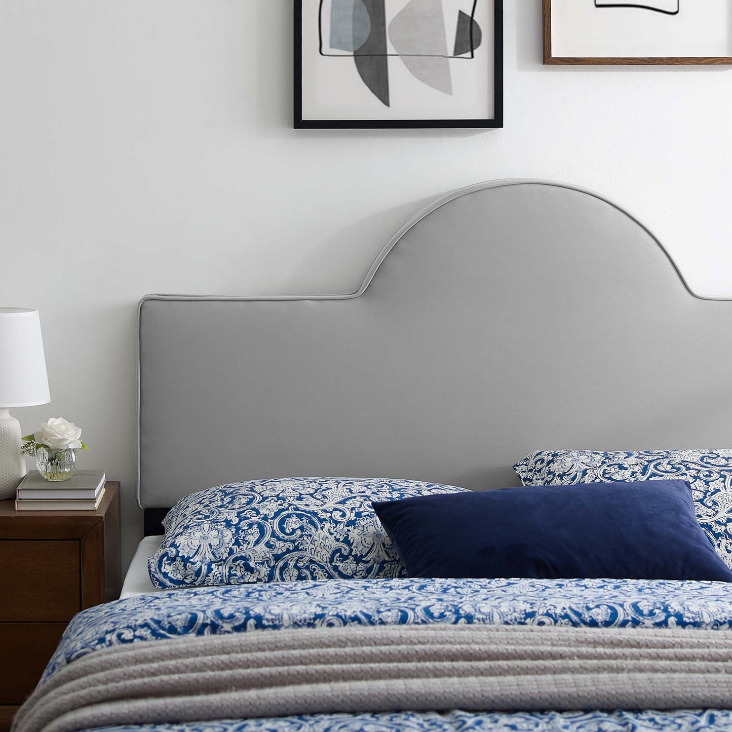 Light gray curved headboard, blue-and-white paisley bedding, navy pillow, wooden nightstand, white lamp.