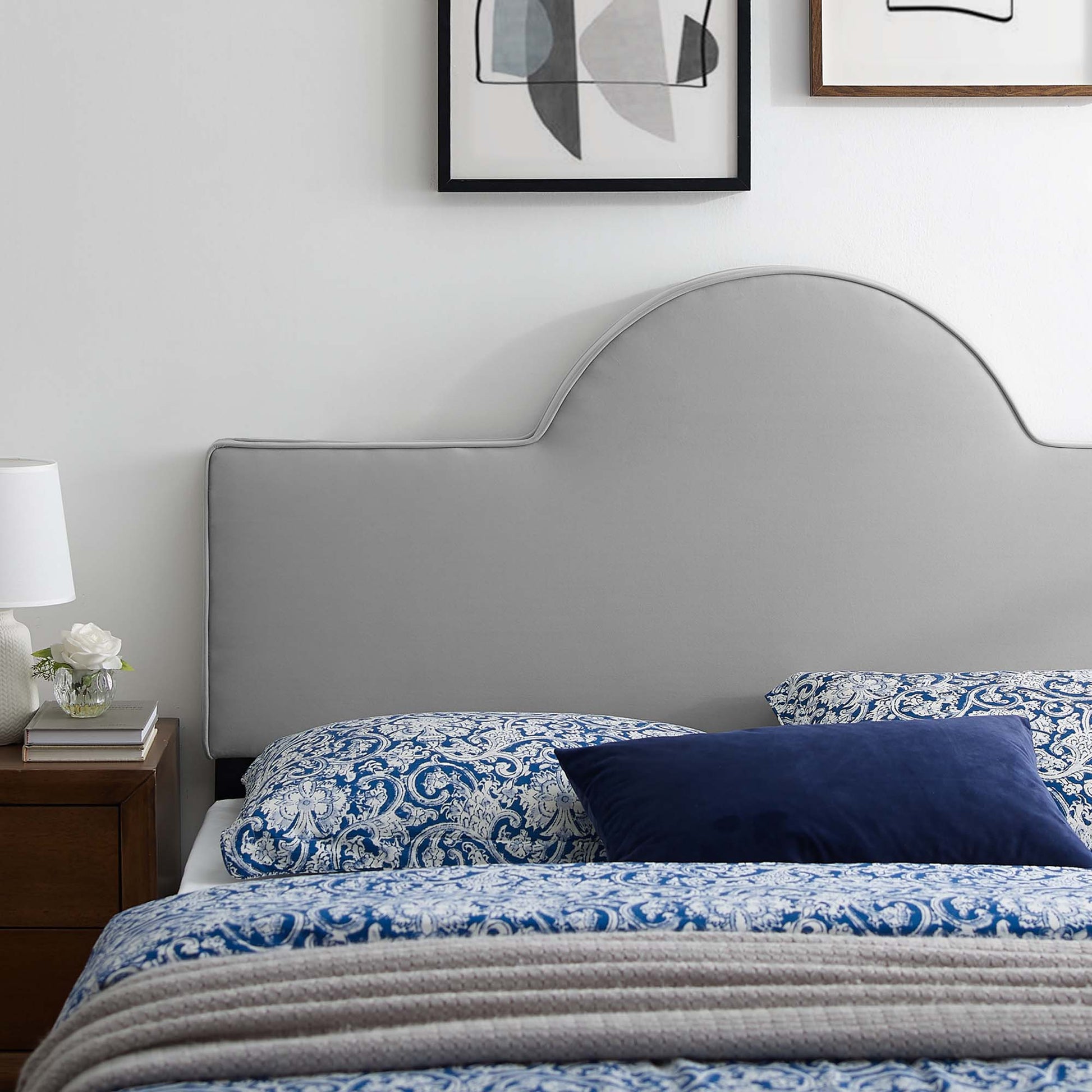 Light gray curved headboard, blue-and-white paisley bedding, navy pillow, wooden nightstand, white lamp.