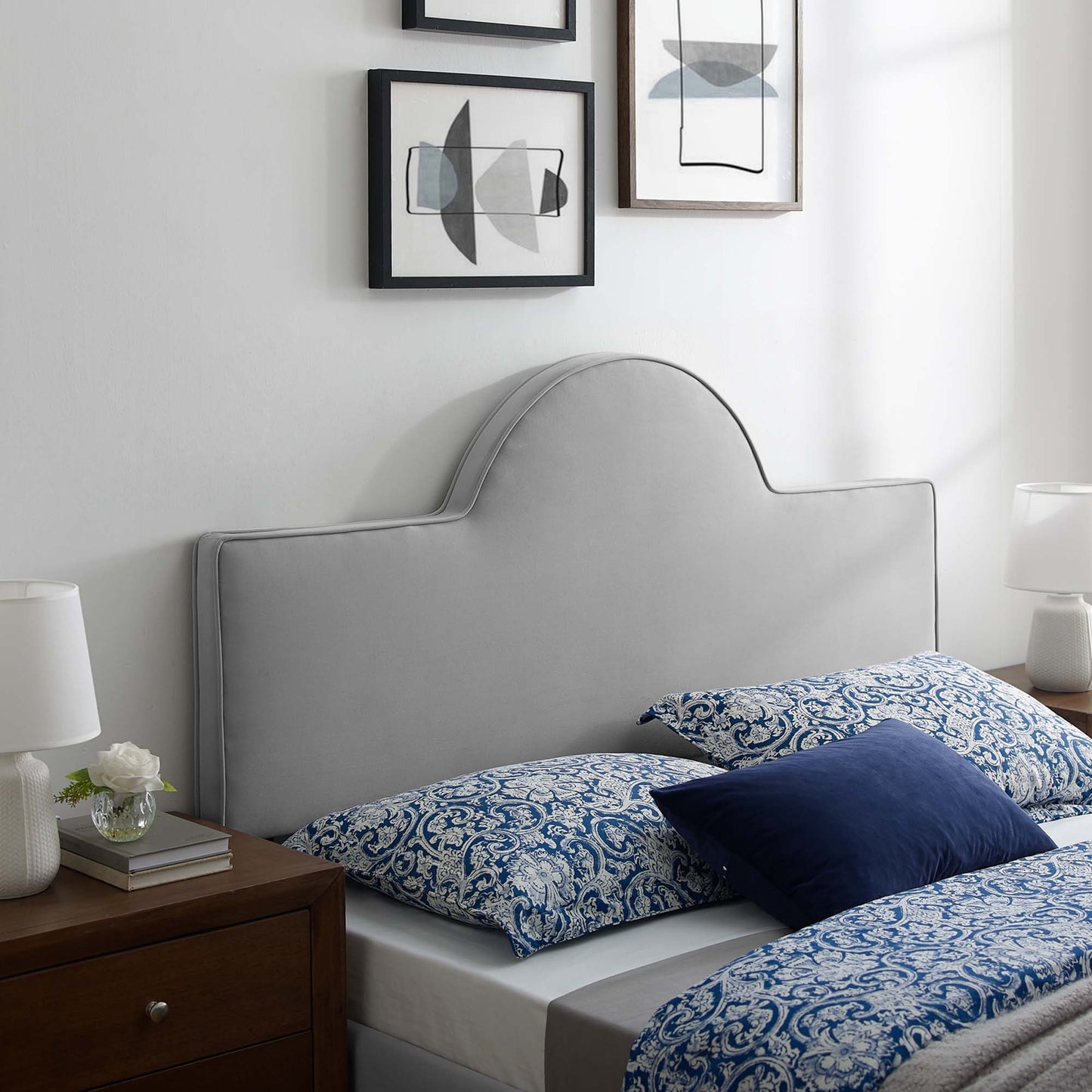 Light gray upholstered headboard with curved top, blue damask bedding, navy pillow, wooden nightstands and lamps