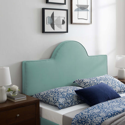 Mint green upholstered headboard with curved arch, blue paisley bedding, dark wood nightstand, white lamps, abstract art.