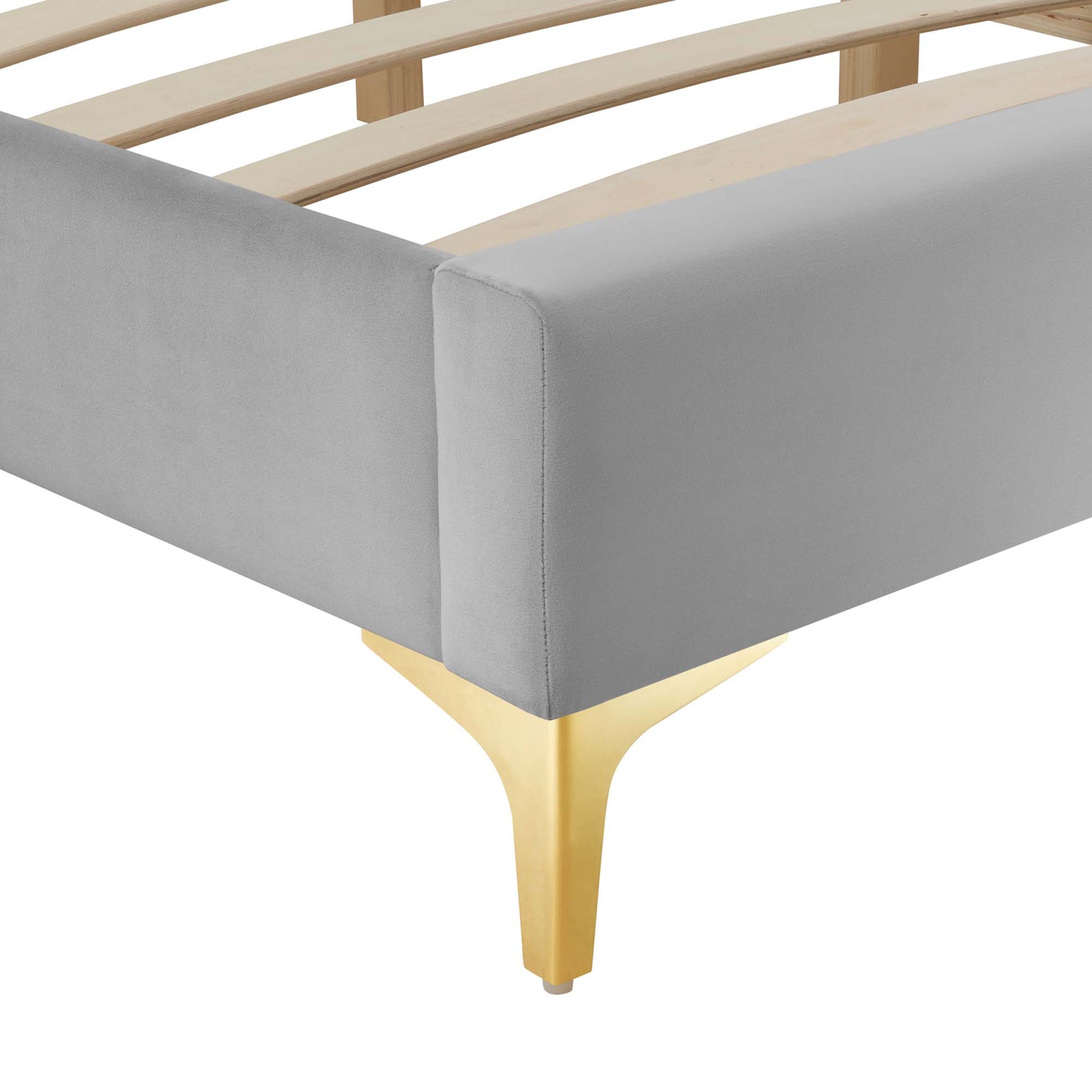Grey upholstered platform bed corner with pale wood slat rails and gold curved metal leg