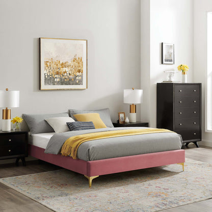 Pink upholstered platform bed with gold legs, gray bedding and yellow throw; black dressers, white lamps, gold-gray art