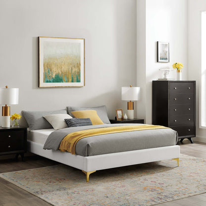 White platform bed with gray bedding, yellow throw, black nightstands, brass lamps, tall dresser, abstract wall art, rug