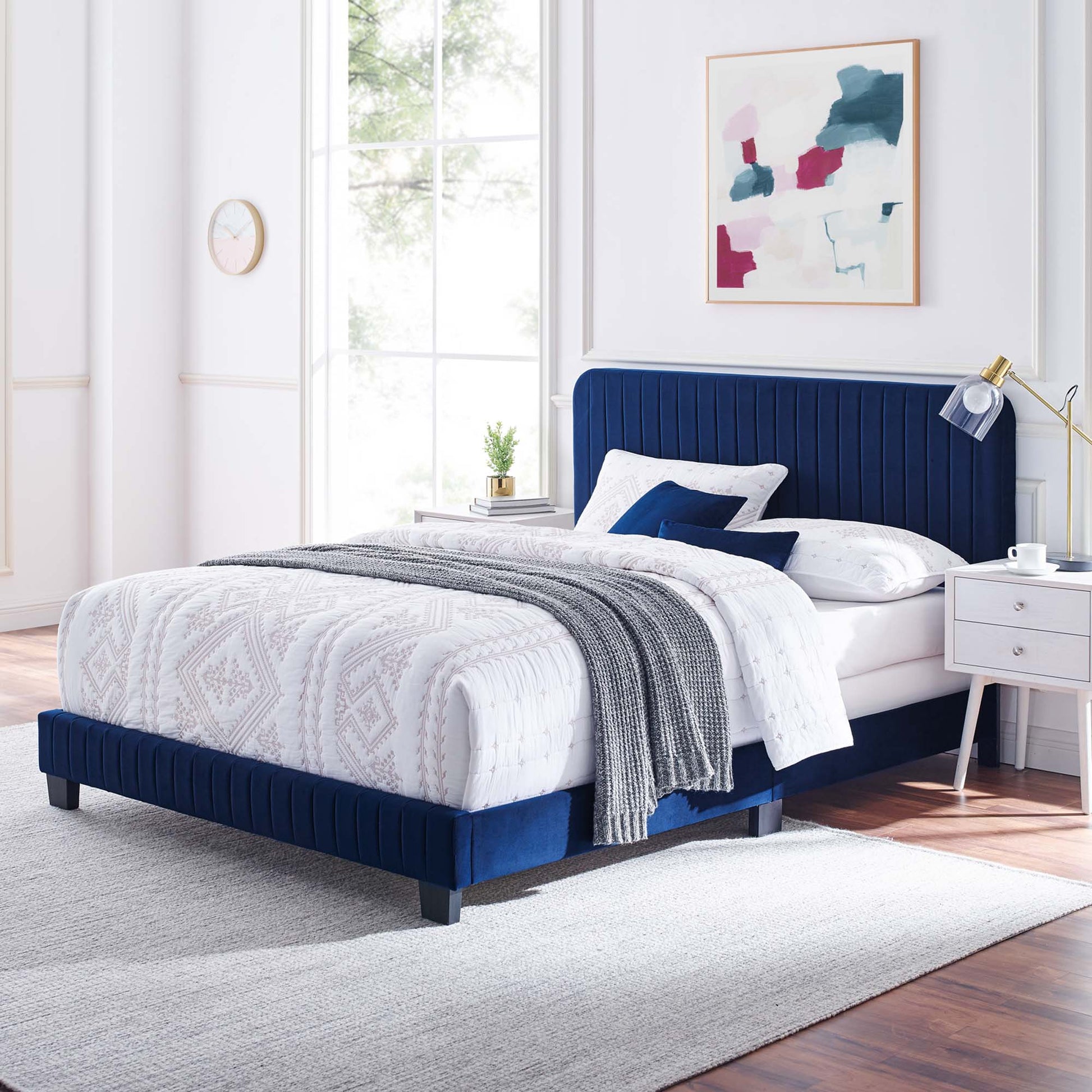 Navy blue upholstered full bed with tufted headboard, white geometric bedding, gray knit throw and navy pillows.