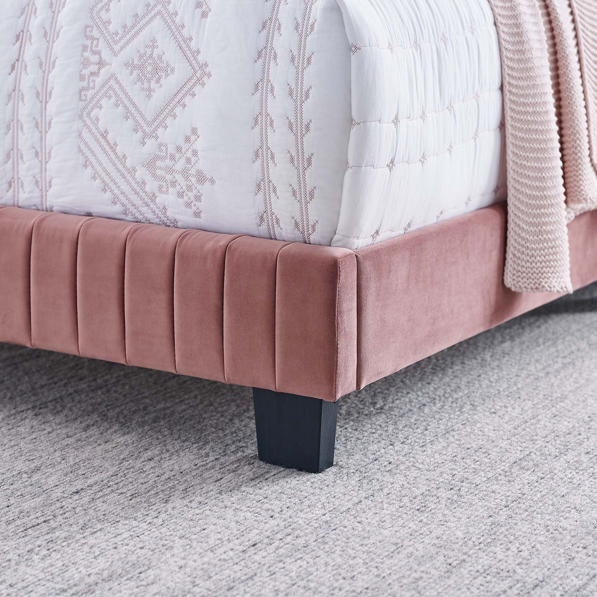 Red velvet twin bed with vertical channel tufting & black block legs, paired with a white embroidered quilt.