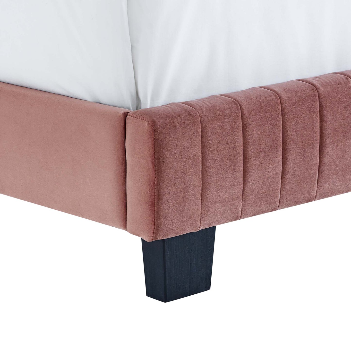 Dusty rose velvet bed footboard with vertical channel tufting and a dark wood block leg.