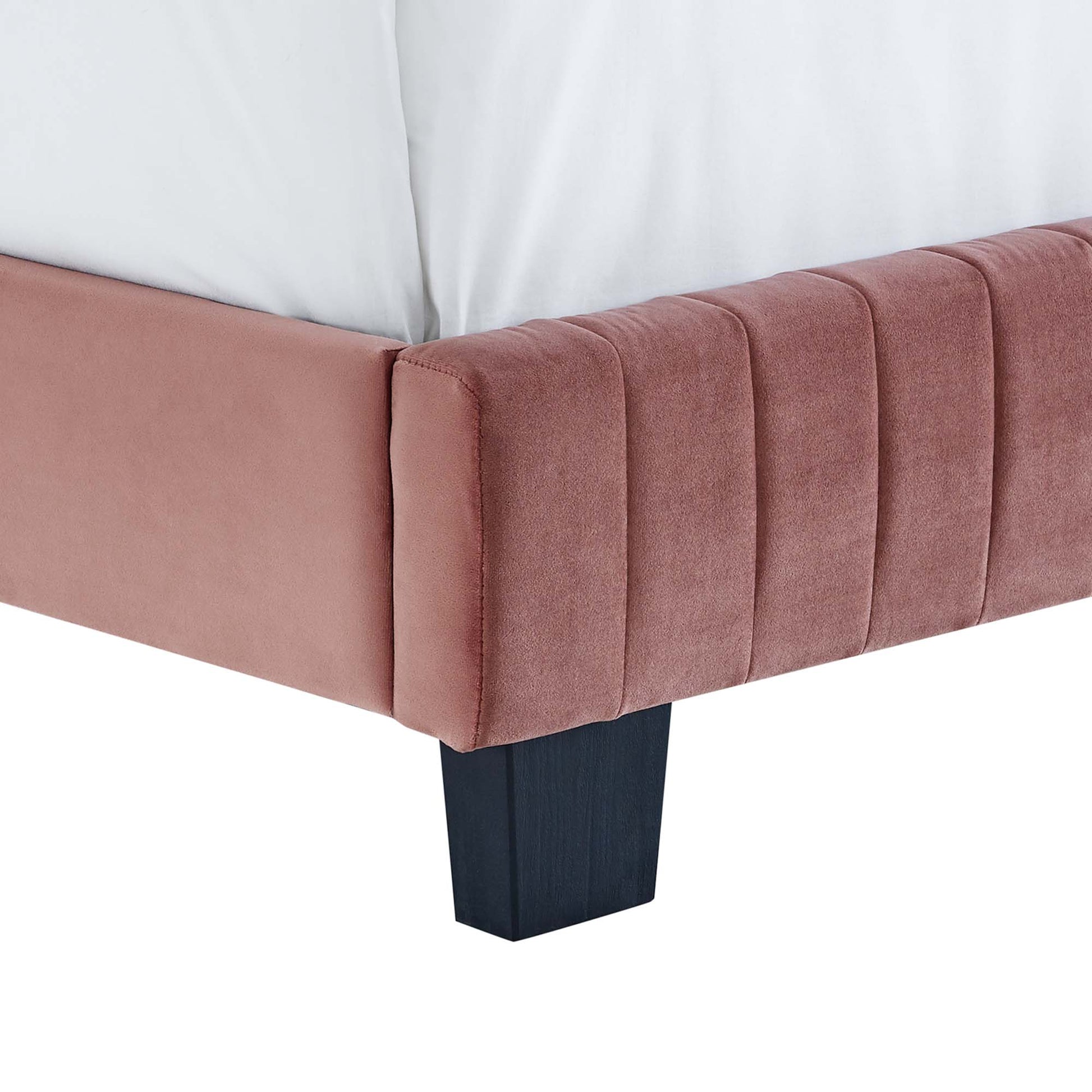 Dusty rose velvet bed footboard with vertical channel tufting and a dark wood block leg.