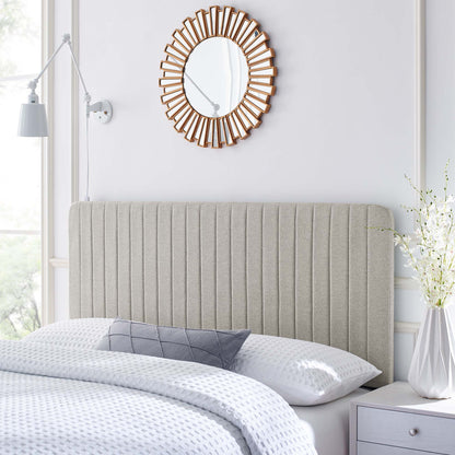 Grey upholstered vertical-channel headboard with white bedding, sunburst wood mirror, white nightstand, vase of flowers.
