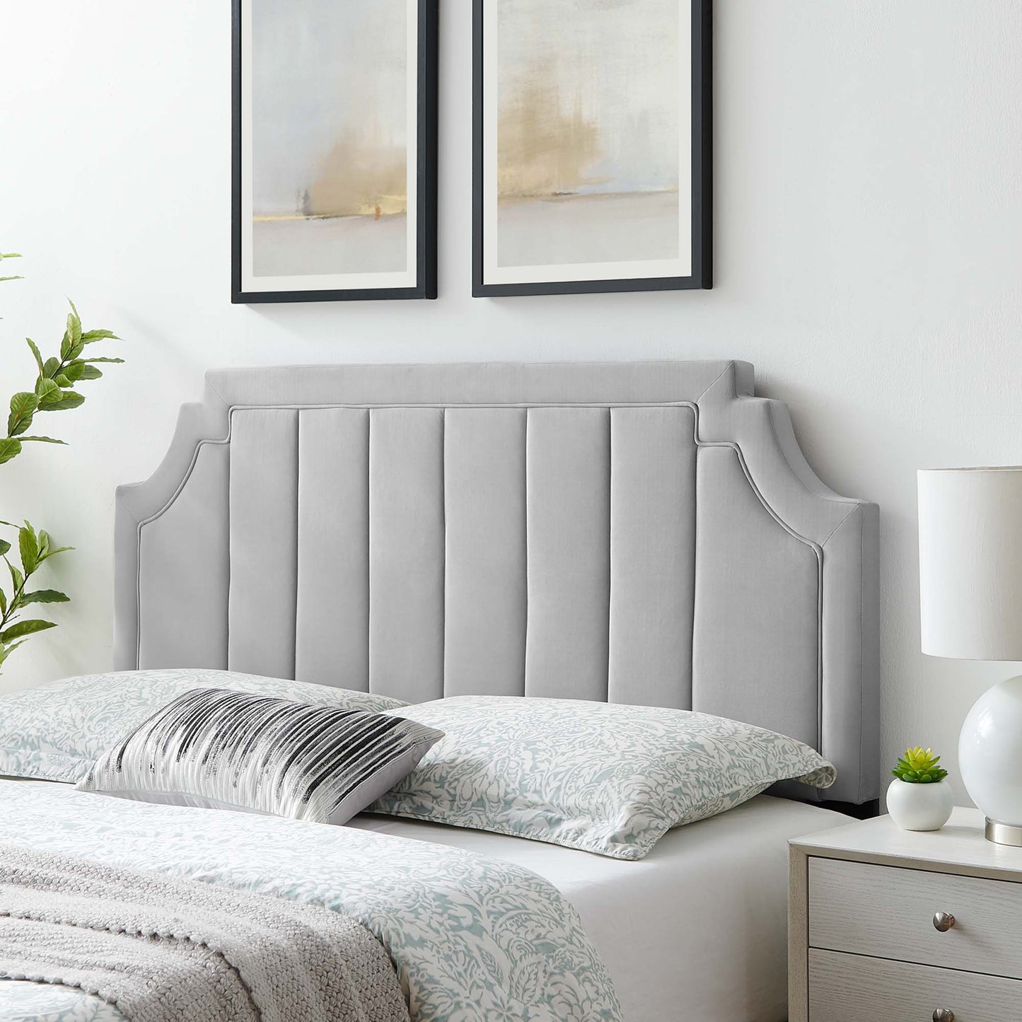 Grey padded upholstered headboard with winged edges and vertical channel stitching, feather-gray bedding and abstract art.