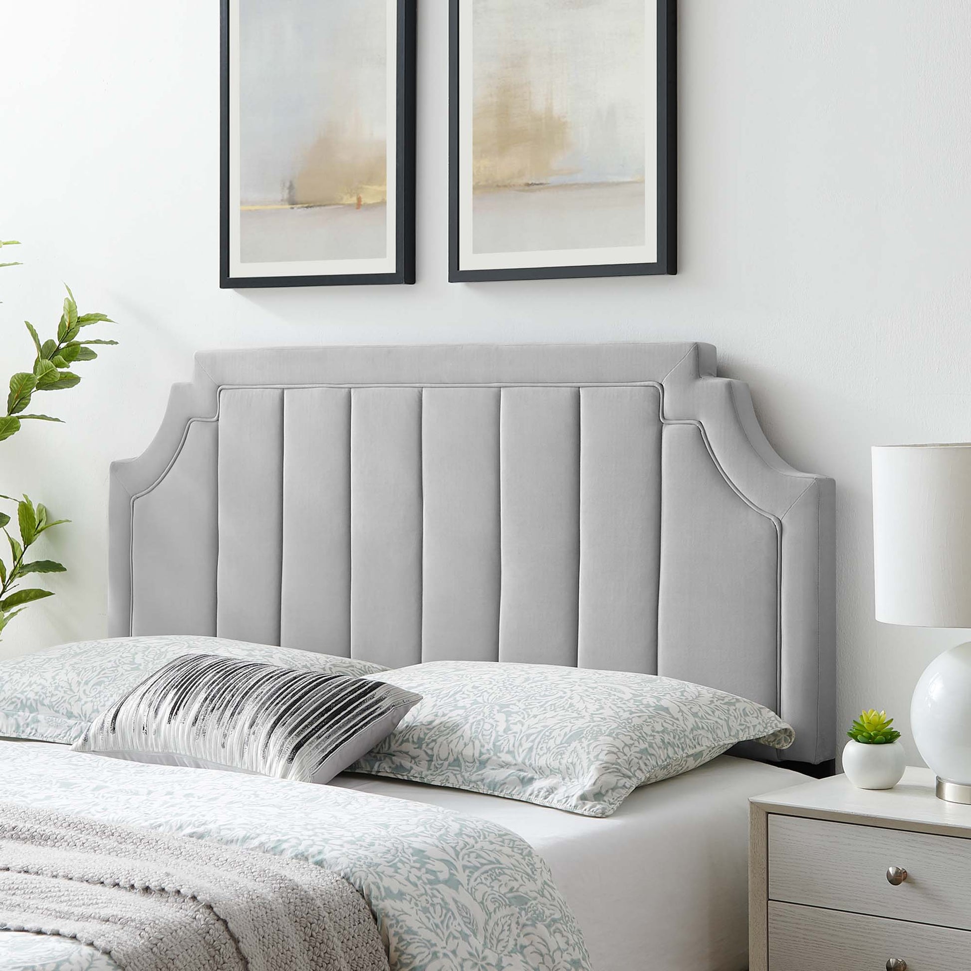 Grey padded upholstered headboard with winged edges and vertical channel stitching, feather-gray bedding and abstract art.