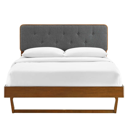 Walnut wood platform bed with charcoal tufted fabric headboard and white bedding, mid-century modern style.